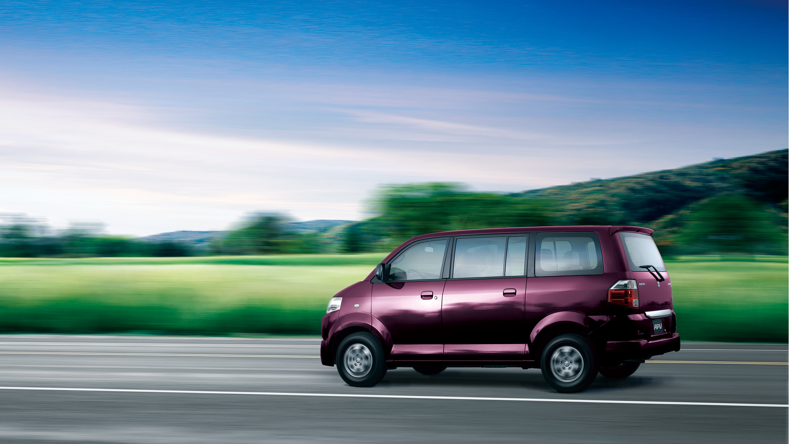 Side-view-of-a-purple-APV-driving-in-green-landscape